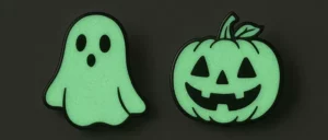 Ghost and pumpkin glow-in-the-dark pins on black background.