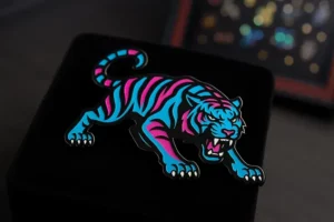 Fierce neon tiger pin with bright blue and pink stripes, snarling and crouched, shown against a black velvet surface.