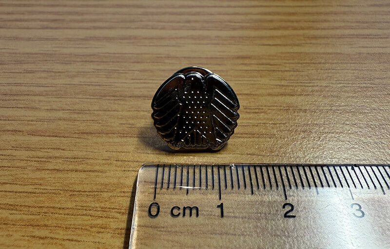 Black metal eagle lapel pin with detailed texture beside ruler